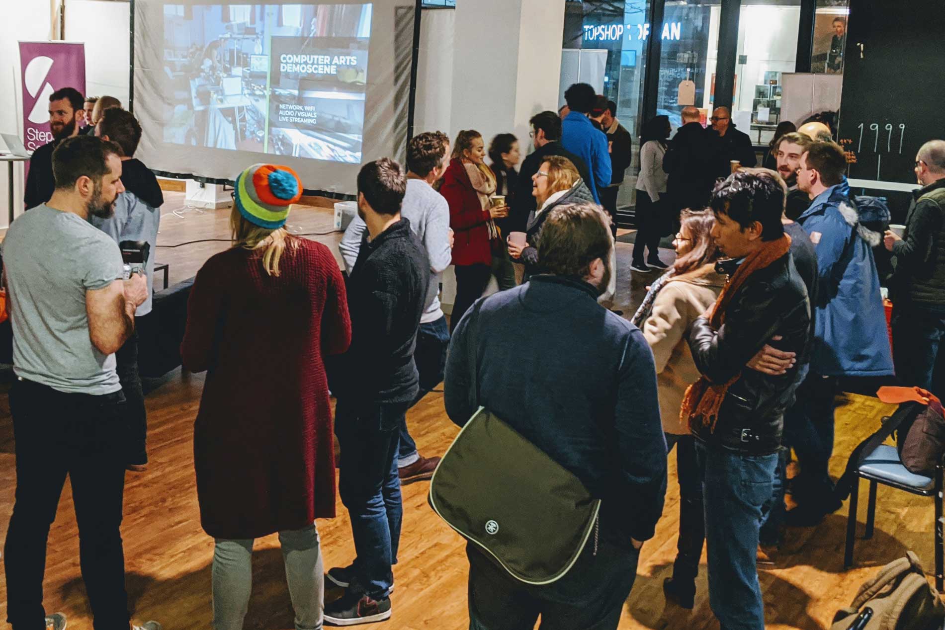 Photo of a group of people mingling with a projector screen in the background